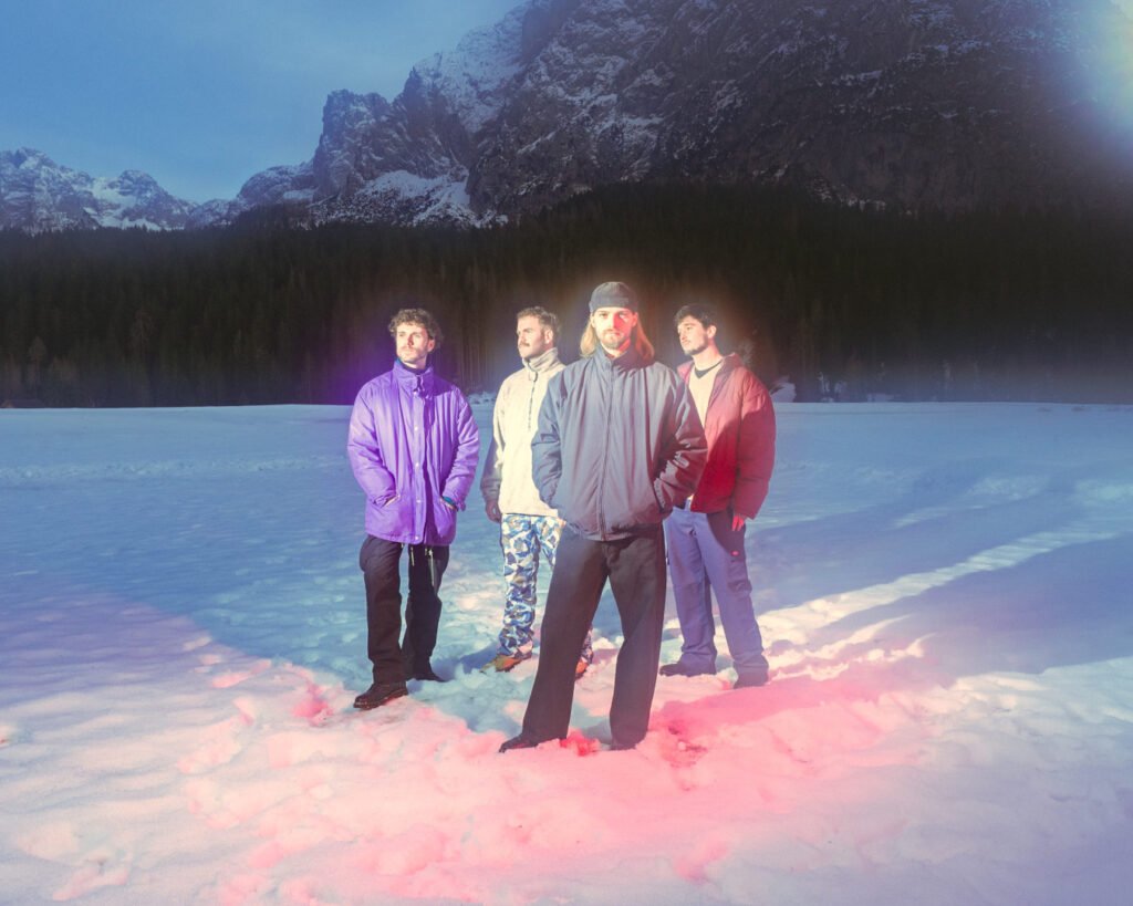 Foto della band Post Nebbia, in primo piano in piedi sulla neve, alle loro spalle un bosco e delle montagne innevate.