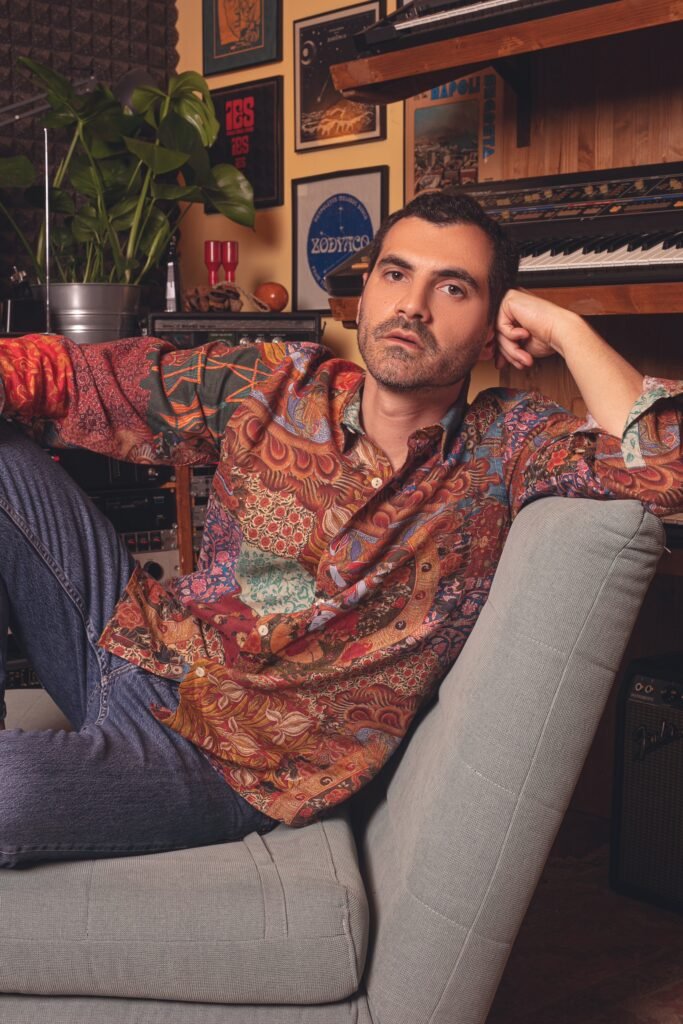 Pellegrino reclinato su una poltrona grigia nel suo studio, con una camicia a fantasia sui toni del rosso scuro