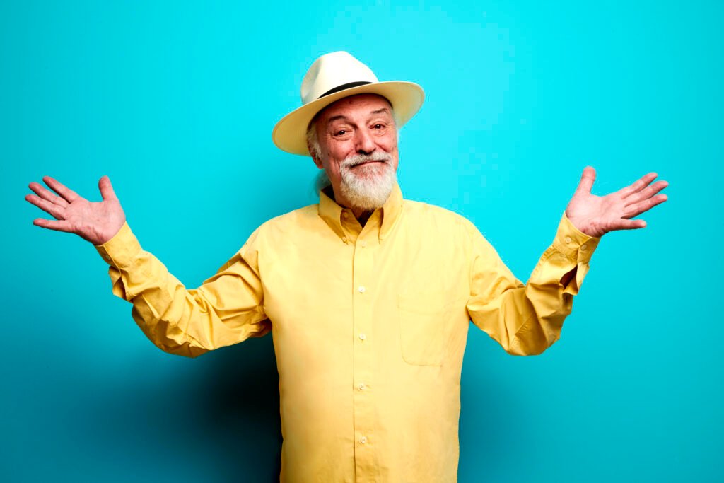 Eugenio Finardi con camicia e panama gialli, che allarga le braccia, su sfondo azzurro.