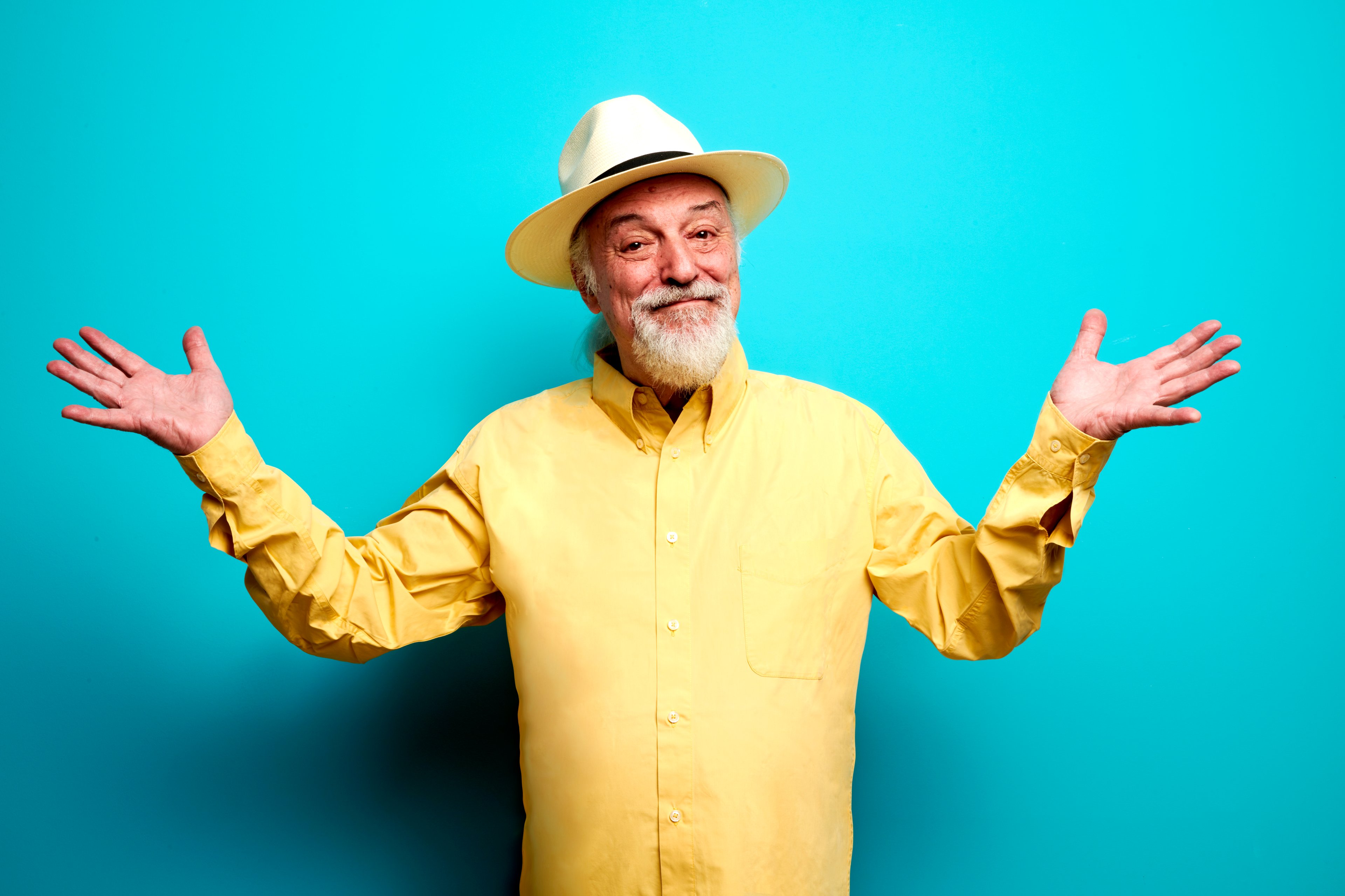 Eugenio Finardi con camicia e panama gialli, che allarga le braccia, su sfondo azzurro.