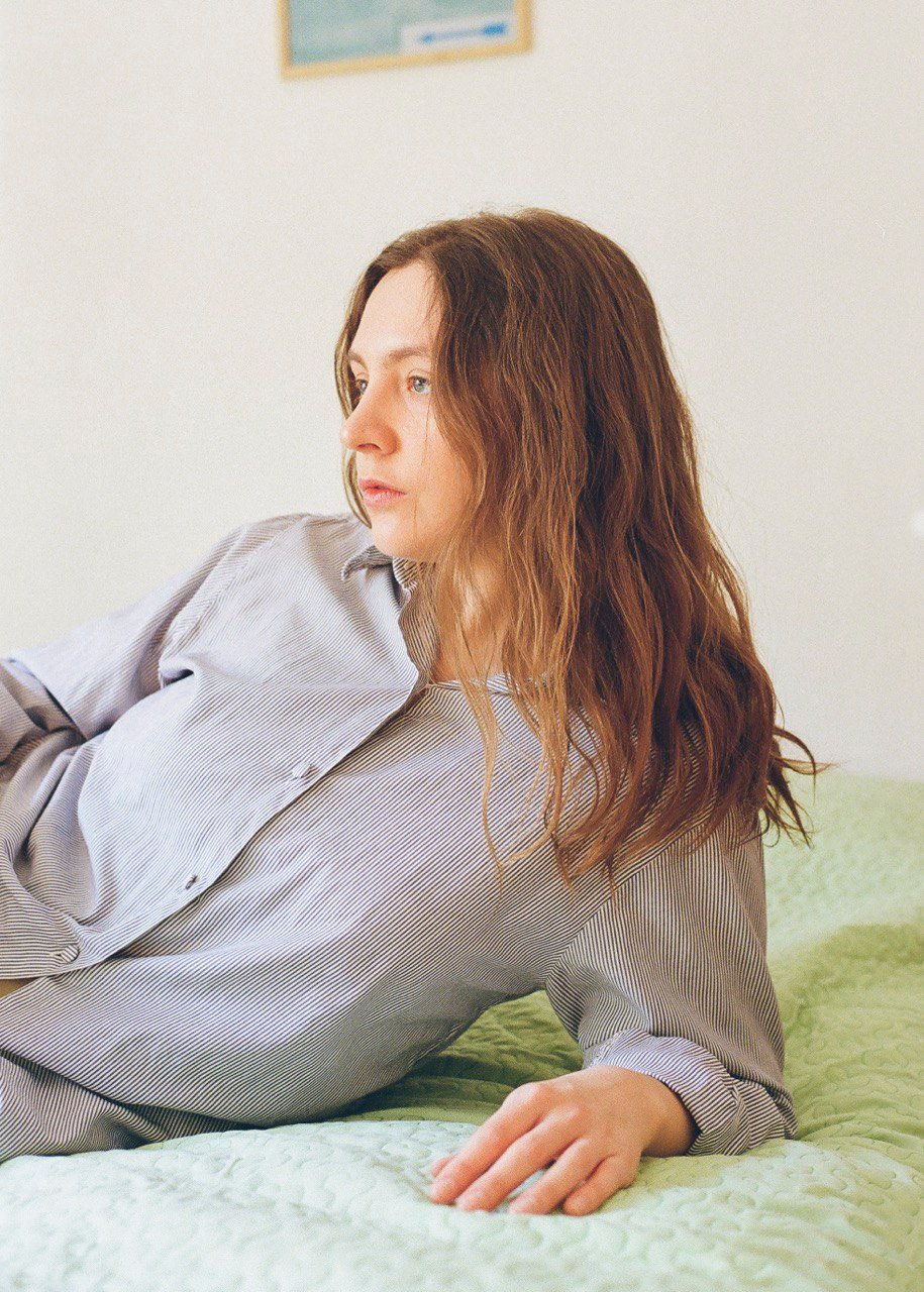 Foto della cantante Any Other reclinata su un braccio, con una camicia grigia ed i capelli sciolti