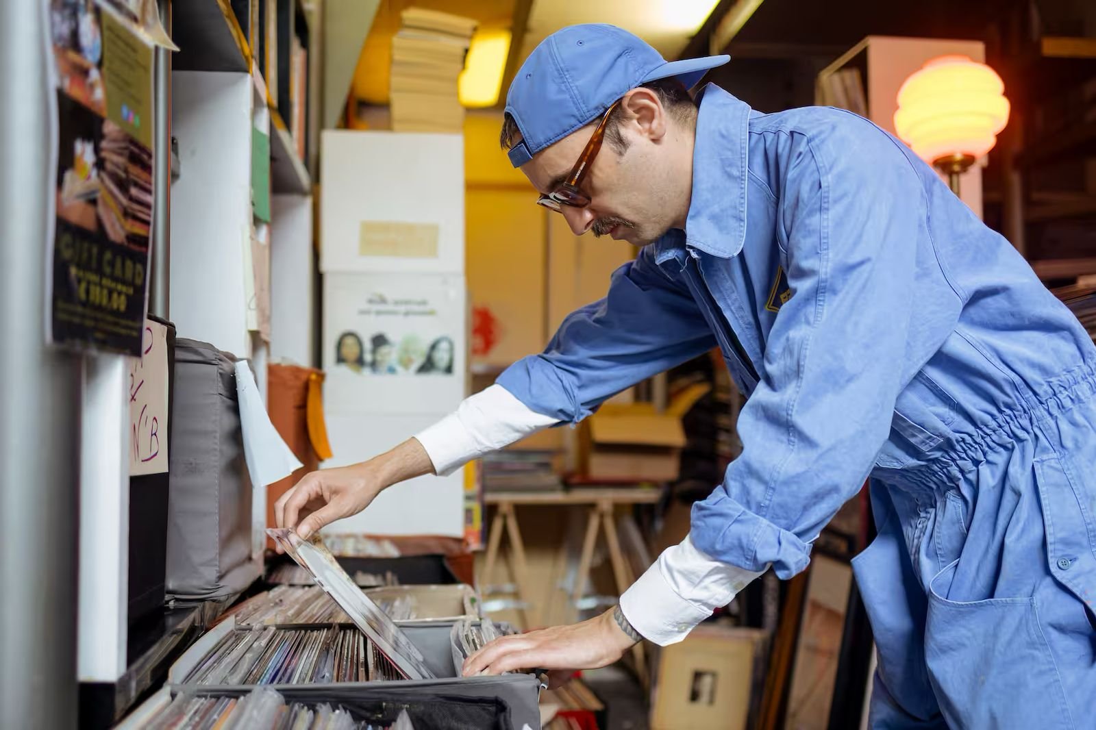 Auoro Borealo con una tuta in denim e cappellino rovesciato in demin, che fruga in una scatola di vinili.