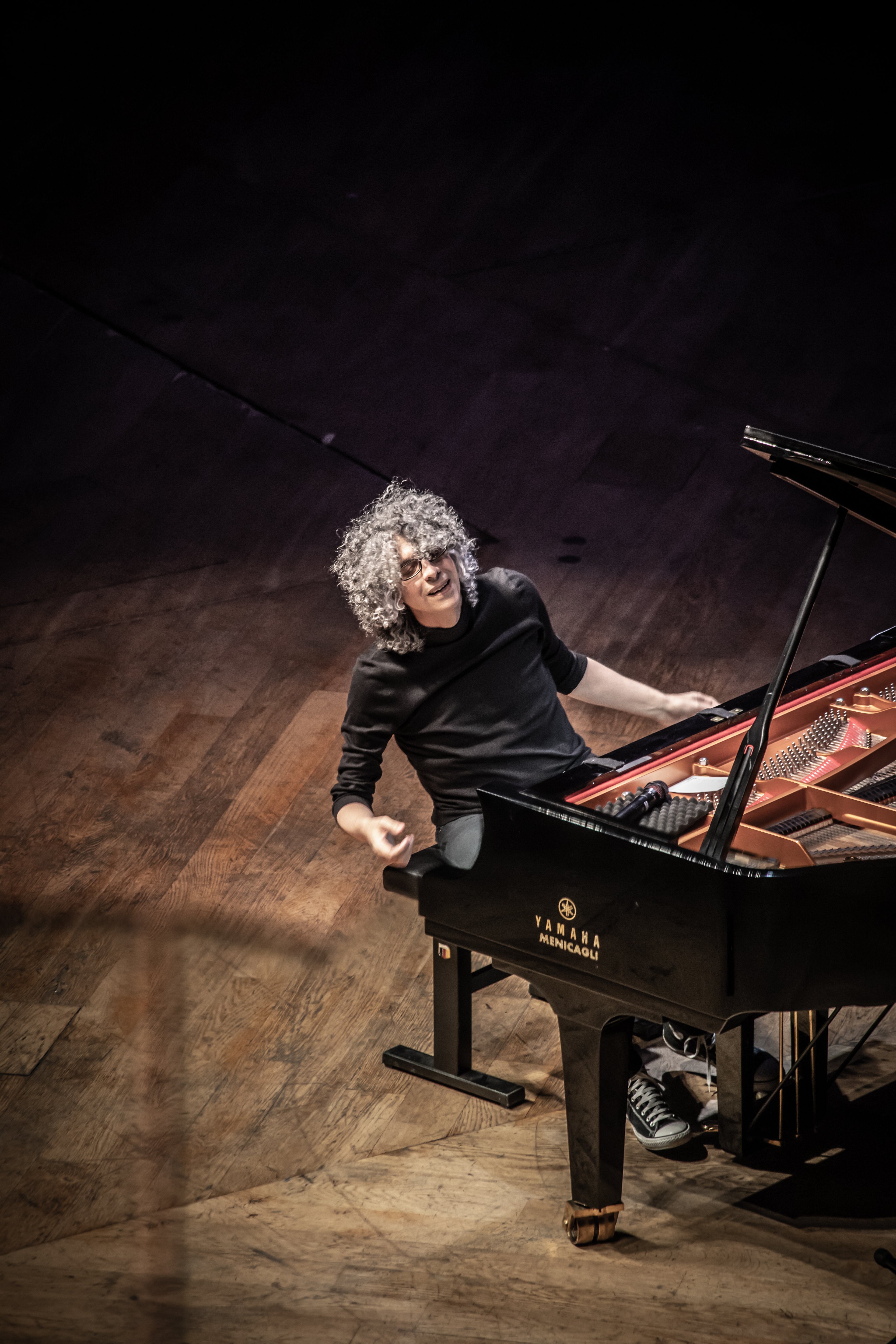 Giovanni Allevi su un palco di legno, al piano, vestito di nero.